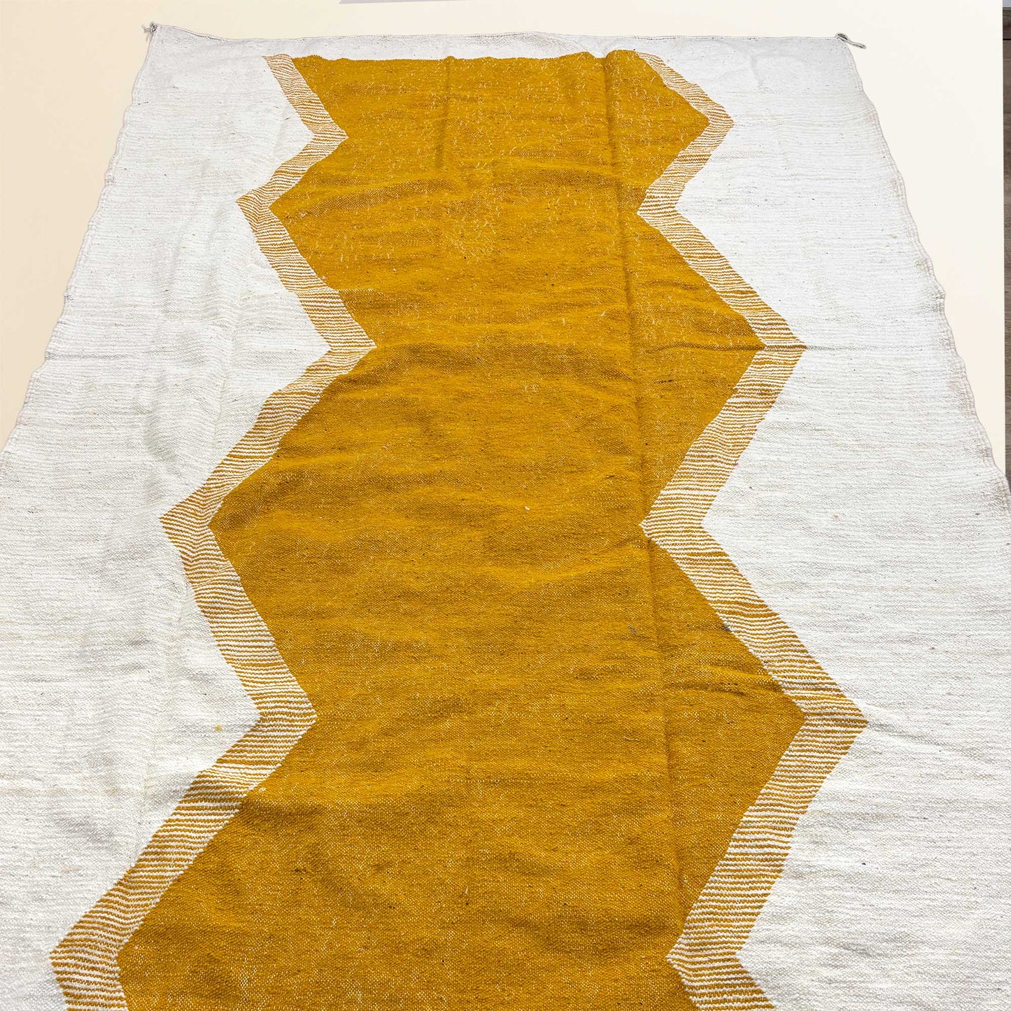 Tapis Kilim Kadhena Solène suspendu, avec grand motif central moutarde sur fond ivoire.