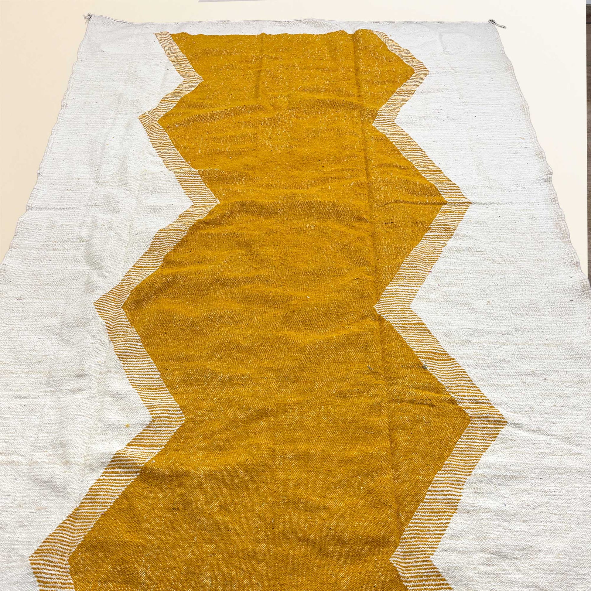 Tapis Kilim Kadhena Solène suspendu, avec grand motif central moutarde sur fond ivoire.