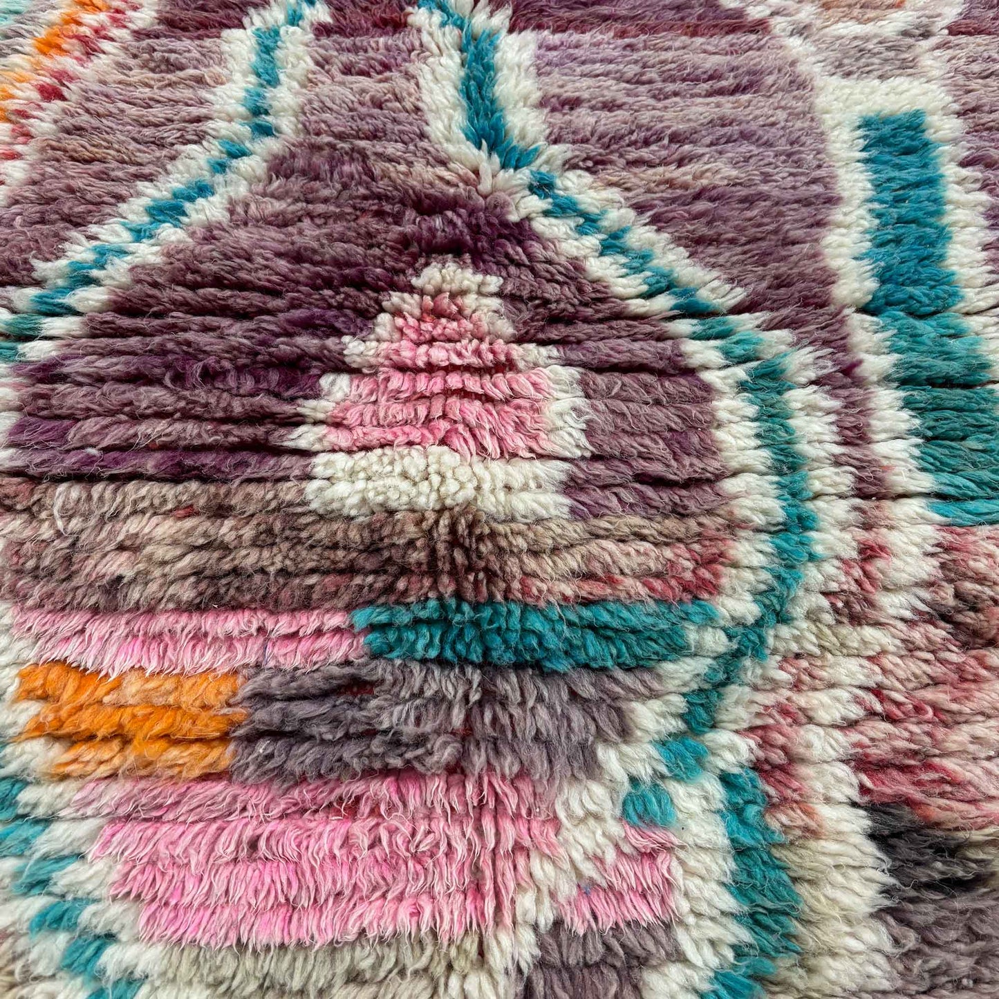 Gros plan sur les motifs abstraits du tapis berbère Kadhena Zélie en rose, lilas et turquoise.