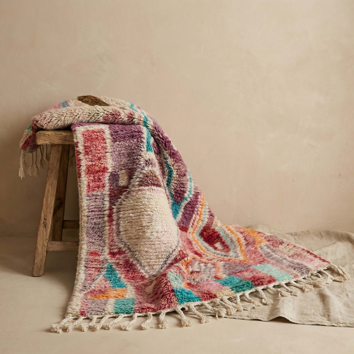 Tapis berbère Kadhena Zélie drapé sur un tabouret dans une ambiance douce et naturelle.
